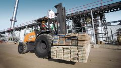 man driving a forklift in a construction site carrying wood planks