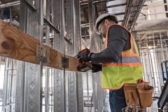 man with a hard hat in fluorescent vest holding a drill posing to do industrial carpentry